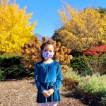 young girl standing in front of autumn trees