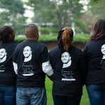 four people with backs turned wearing t-shirts with photograph memorial on them