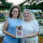 two women holding floating lanterns with family photos outside in front of fountain