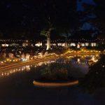 people sitting outside next to a fountain with string lights