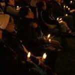 people sitting in chairs outside at night holding candles