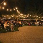 people sitting in chairs outside at night with string lights