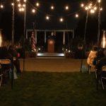 speaker at podium outside at night with string lights and chairs