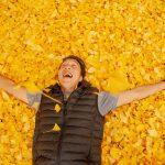 man laying in pile of yellow and orange leaves with arms out