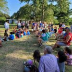 group of people sitting around outside listening to a bee keeper speak