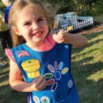 young girl holding a popsicle stick with fresh honey on it