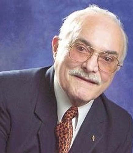 Older man in suit posing in front of a blue backdrop