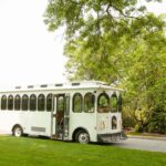 photo of an old fashioned trolley on a road with trees in the background