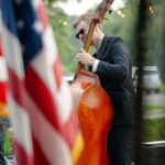 man framed by an American flag playing the cello