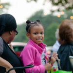 little girl smiling at camera with family outside