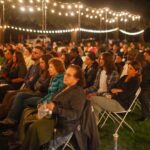 group of people sitting outside in chairs holding candles