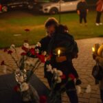 woman holding small child placing a rose into a vase holding a candle