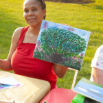 woman smiling holding canvas with painting on it