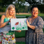 two women holding up a painted canvas together