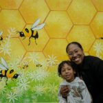 woman and young boy smiling in front of a beehive backdrop