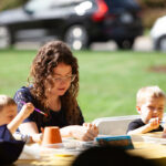 woman with two young children doing an art project outside