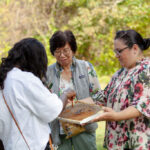 women standing with a sheet of honey comb trying honey